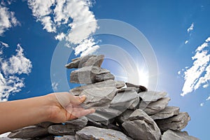 Woman adds rock to cairn under sun filled sky