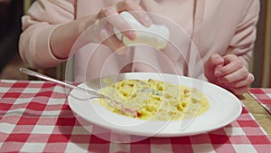 A woman adds salt or pepper to a pumpkin pasta with a shrimps, cherry tomatoes and basil.
