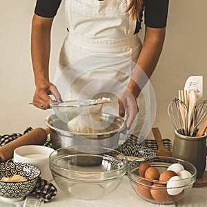 Woman adds some flour to dough on wooden table. Woman hands kneading fresh dough.