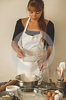 Woman adds some flour to dough on wooden table. Woman hands kneading fresh dough.