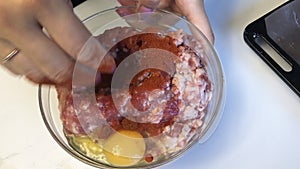 The woman adds the spices in a container with minced meat and chicken egg, and then mixes the contents.