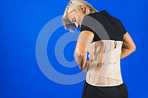 woman adjusting corset on her back to support her back from pain in the back and spine, blue background