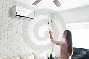 Woman Adjusting Temperature Of Air Conditioner With Remote