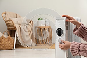 Woman adjusting temperature on modern portable electric heater indoors, closeup. Space for text