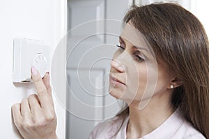 Woman Adjusting Thermostat On Central Heating Control