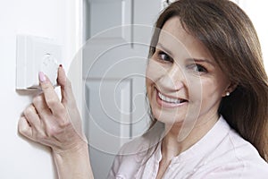 Woman Adjusting Thermostat On Central Heating Control