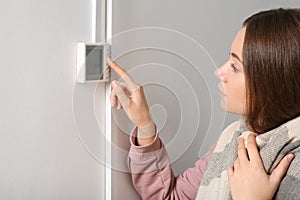 Woman adjusting thermostat on white wall.