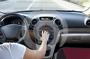 Woman adjusting volume at car audio system while she is driving.