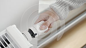 A woman adjusts the radiator thermostat to the maximum temperature in the room