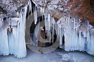 A woman admires huge icicles in an ice cave. Winter trip on the frozen Lake Baikal.
