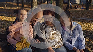 Woman with adult son and his daughters sitting on a bench in the Park and watching photos on smartphone. The link