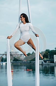 Woman aerialist performs acrobatic tricks on hanging aerial silk