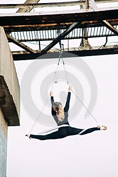 Woman aerialist performs gymnastic split on aerial silk attached to the bridge