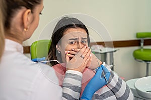 Woman afraid before dentisr procedure and covering mouth her hands, panic attack to pain