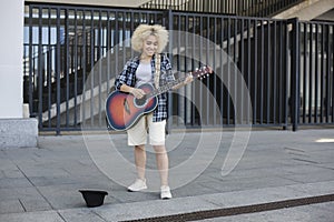 Woman African-American appearance, street musician earns money by playing the guitar