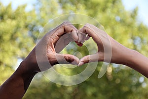 Woman and African American man making heart with hands outdoors, closeup