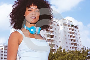 Woman with afro hairstyle with blue headphones. Buildings, sky a