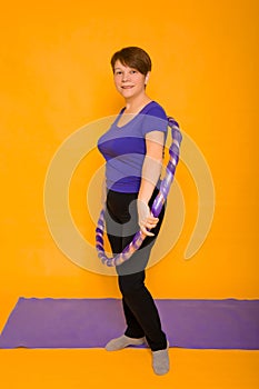 The woman at the age holds in hands a hoop for gymnastics standing on a rug. Studio photo on a yellow background