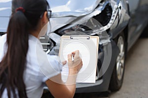 Woman agent filling out insurance claim form near wrecked car closeup