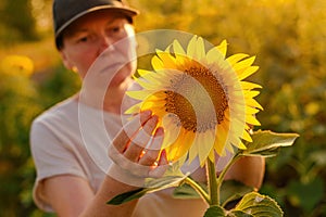 Woman agronomist and farm worker wearing trucker\'s hat examining crops in blooming sunflower field. Agriculture and farming