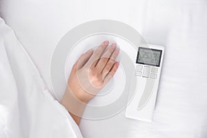 Woman with air conditioner remote control bed, focus on hand