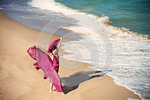 Woman in airy crimson dress on the beach
