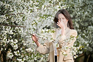 Woman allergic suffering from seasonal allergy at spring in blossoming garden at springtime.