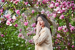 Woman allergic suffering from seasonal allergy at spring in blossoming garden at springtime.