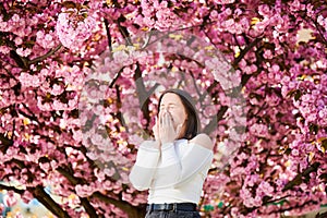 Woman allergic suffering from seasonal allergy at spring in blossoming garden at springtime.