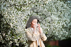 Woman allergic suffering from seasonal allergy at spring, sneezing, blowing nose with handkerchief.