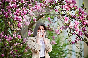 Woman allergic suffering from seasonal allergy at spring, sneezing, blowing nose with handkerchief.