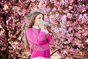 Woman allergic suffering from seasonal allergy at spring, sneezing, blowing nose with handkerchief.