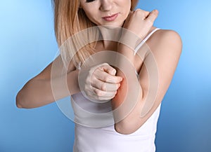 Woman with allergy symptoms scratching forearm on color background