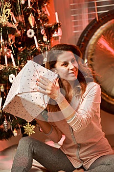 Woman alone at home at Christmas, opening a present by the Christmas tree