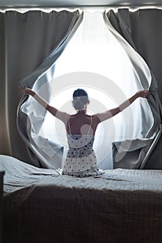 Woman alone at home , opens the curtains letting in bright ray of sunlight