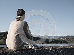 Woman alone sitting on stone coast and looking at sea and mountan