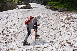 Woman alpinist with ice axe, crampons and backpack, stops and smiles on late Summer snow, in the White Valley.