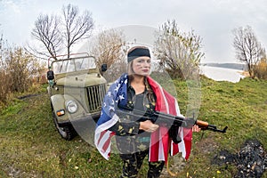 Woman with american flag and rifle near military car