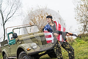 Woman with american flag and rifle near military car