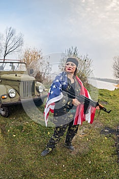 Woman with american flag and rifle near military car