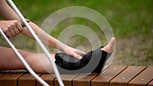 Woman with ankle brace holding crutch sitting outdoors, trauma bandage, health