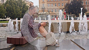 Woman is anxiously using the phone at the city fountain.