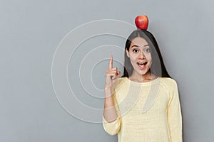 Woman with apple on head pointing up and having idea