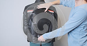 A woman applies a back protector to a leather motorcycle sport jacket worn by a biker. Moto accessories, saving the life