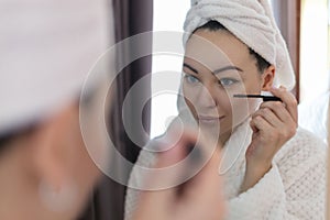 A woman applies black mascara to her eyelashes with a makeup brush. Young