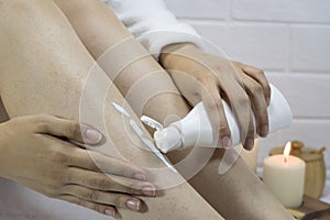 A woman applies a moisturizer to the skin of her legs. Problem skin, strawberry legs, chicken skin, hyperkeratosis, keratosis