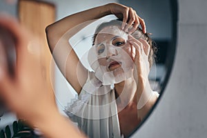 Woman applies sheet mask to her face in the bathroom