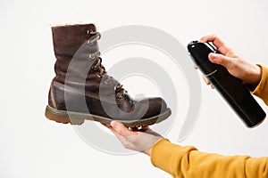 A woman applies the spray to brown nubuck women& x27;s winter boots. Water-repellent care for shoes, renewal and