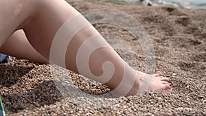 Woman applies sunscreen on leg sitting on sea pebble beach