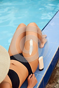 Woman apply sun cream protection cream on her smooth tanned legs. Beautiful legs outdoors by pool.